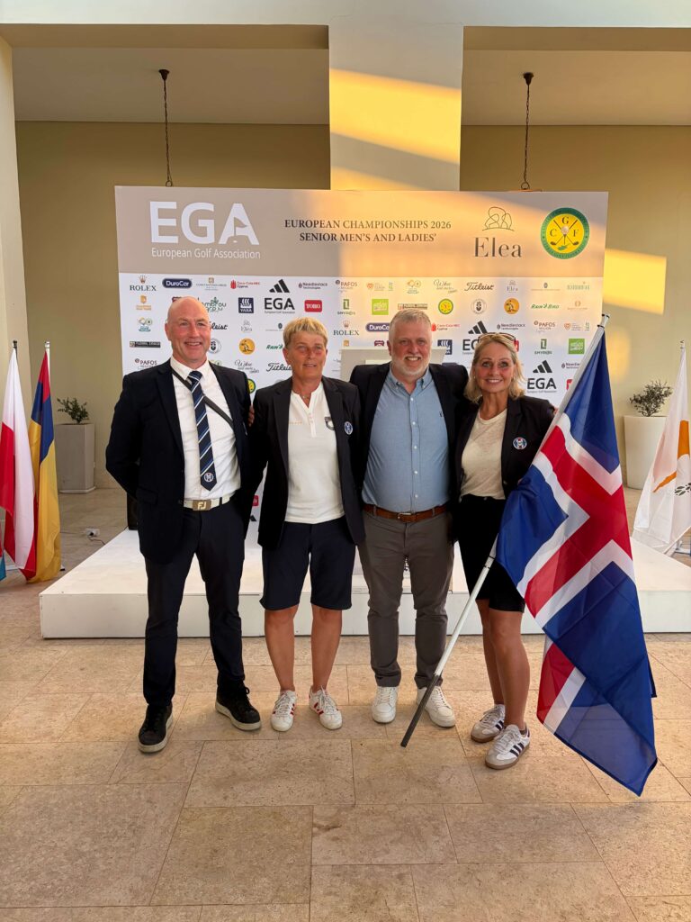 Four adults in smart casual clothing pose for a photo in front of a sponsor wall at the European Golf Association event, with flags nearby.