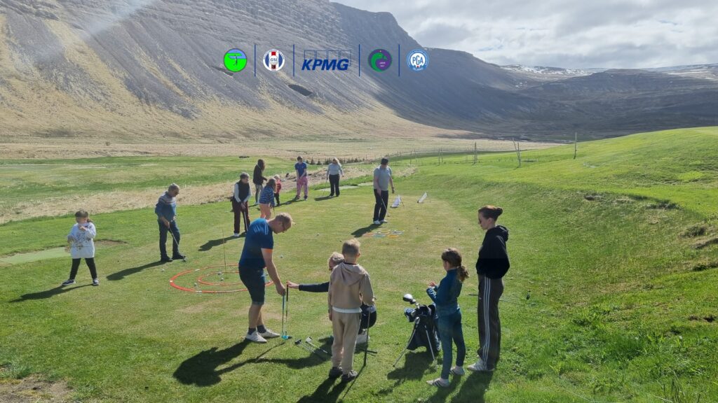 Group of adults and children playing golf on a grassy field with mountains in the background; equipment and colorful rings laid out on the ground, weather sunny and clear.