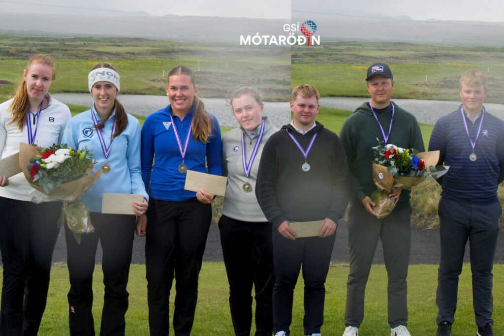 Seven young athletes stand in a row wearing medals, some holding bouquets and envelopes, outdoors with a grassy field and water behind them, logo above.