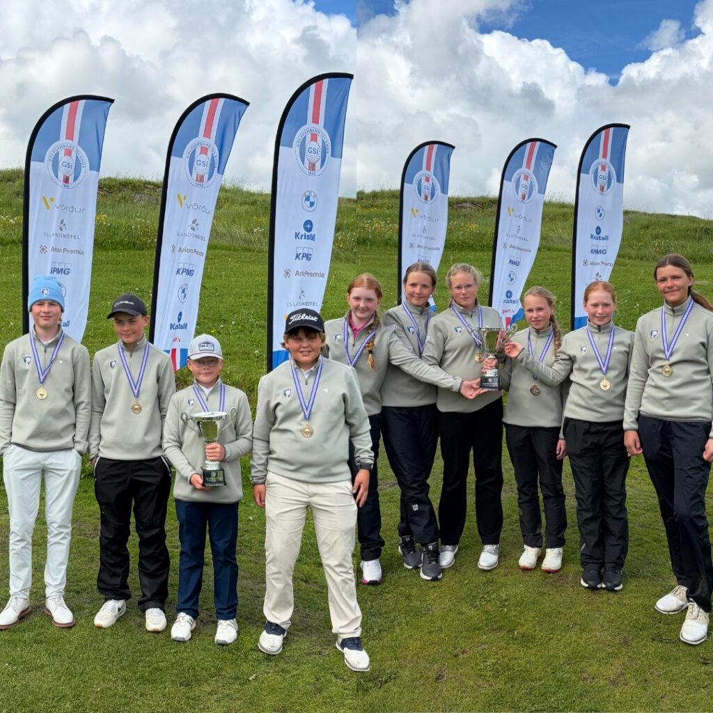 Group of young athletes outdoors, wearing gray sweatshirts and medals, holding trophies in a grassy field with sponsor banners behind them.